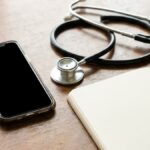 A smartphone, stethoscope and notebook on a consultation desk