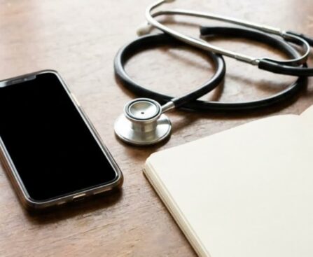 A smartphone, stethoscope and notebook on a consultation desk