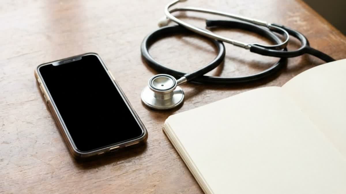 A smartphone, stethoscope and notebook on a consultation desk