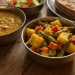 A plate of Indian dal, mixed vegetable sabzi and roti on a wooden table