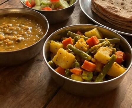 A plate of Indian dal, mixed vegetable sabzi and roti on a wooden table
