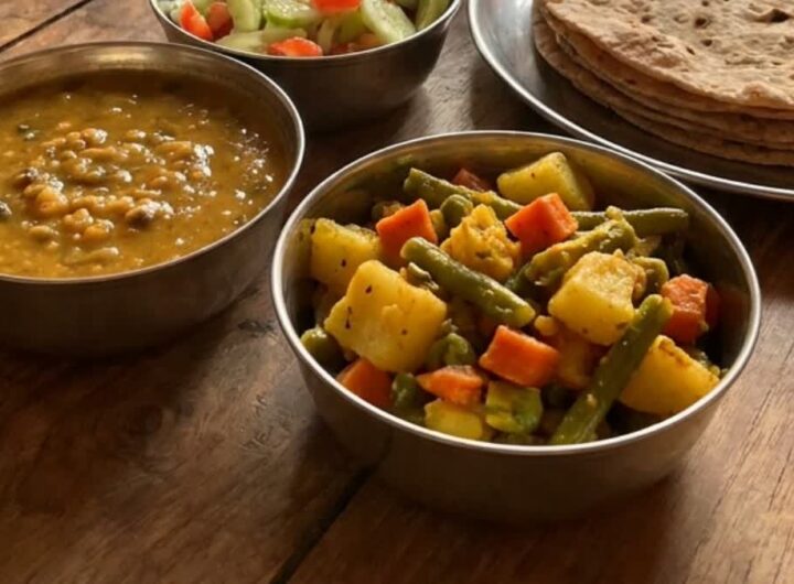 A plate of Indian dal, mixed vegetable sabzi and roti on a wooden table
