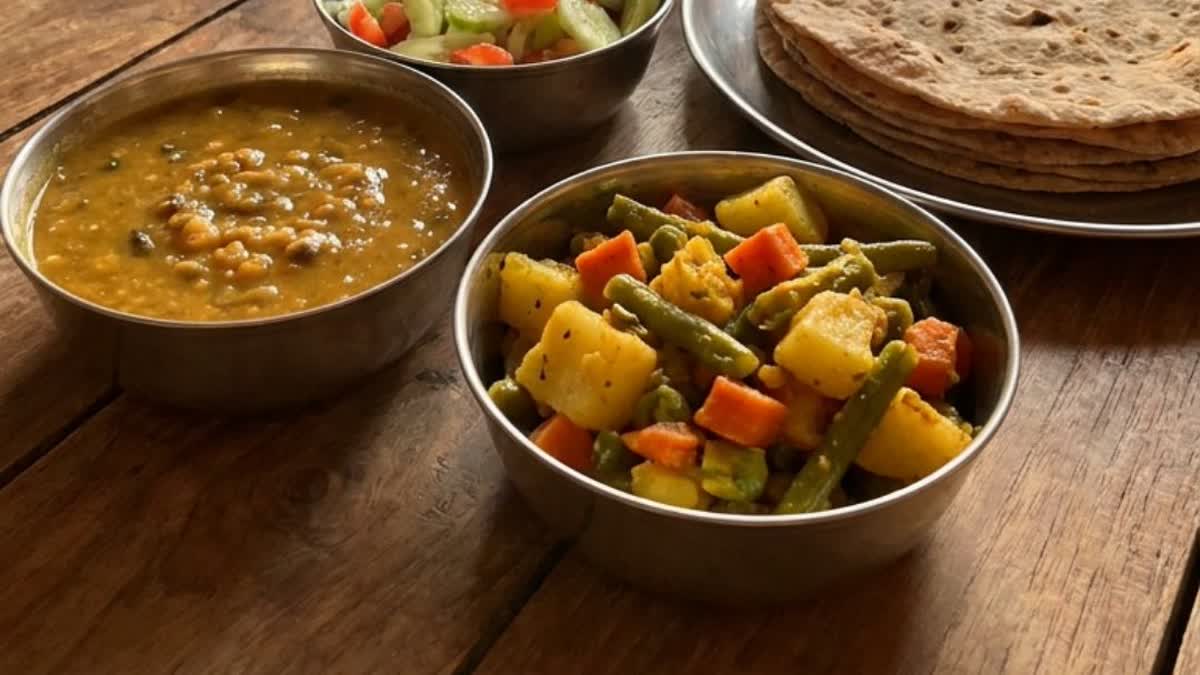 A plate of Indian dal, mixed vegetable sabzi and roti on a wooden table