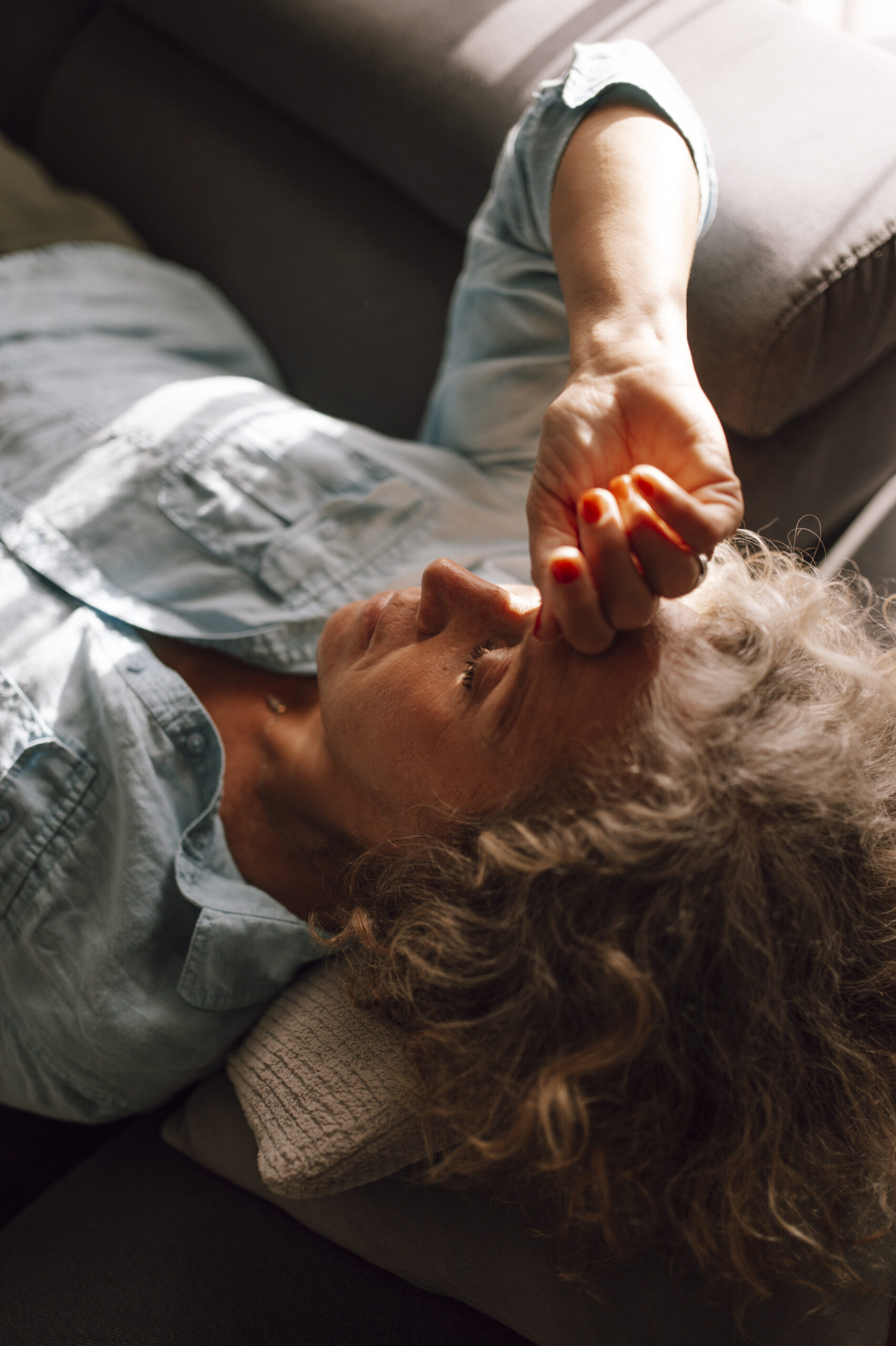 Woman resting on a couch with her hand on her forehead, expressing stress